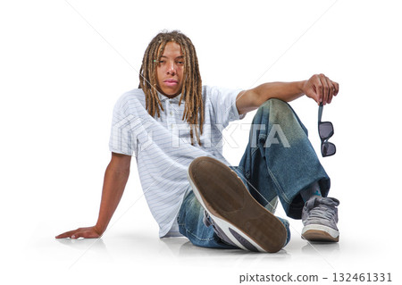Young man with dreadlocks sitting on floor holding sunglasses 132461331
