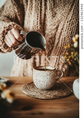 Faceless person in a cozy sweater pouring coffee into a ceramic cup. A warm and minimal moment of morning calm. 132461448