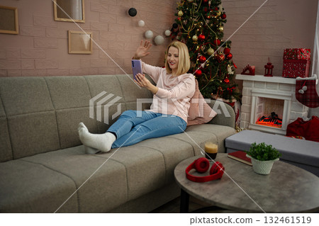 Joyful woman enjoying a virtual chat by the festive tree in a cozy living room decorated for the holidays Joyful woman enjoying a virtual chat by the festive tree in a cozy living room decorated for the holidays 132461519