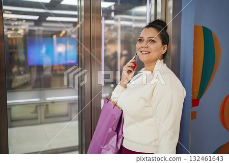 Smiling woman enjoys a phone call while holding shopping bags Smiling woman enjoys a phone call while holding shopping bags 132461643