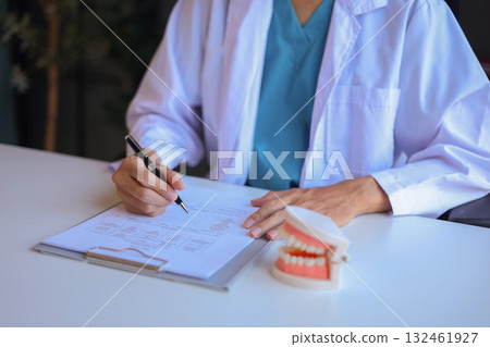 Dentist uses a dental model to explain oral health and treatments to a patient. 132461927