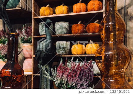 Fluffy orange pumpkins made from textile material displayed alongside mossy planters and glass vases. Thanksgiving home styling, cozy seasonal textures, decorative foliage, rustic holiday interior 132461961