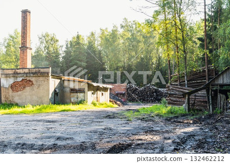 Abandoned industrial site with weathered buildings, a tall chimney, and stacked logs surrounded by lush greenery, showcasing a blend of nature and decay in a serene environment Abandoned industrial site with weathered buildings, a tall chimney, and stacked logs surrounded by lush greenery, showcasing a blend of nature and decay in a serene environment 132462212