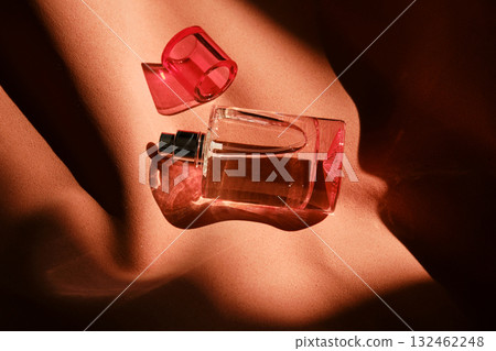 A pink perfume bottle on a soft reddish background. A pink perfume bottle on a soft reddish background. 132462248