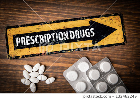 Prescription drugs concept with yellow arrow sign and white pills in blister packs on wooden table Prescription drugs concept with yellow arrow sign and white pills in blister packs on wooden table 132462249