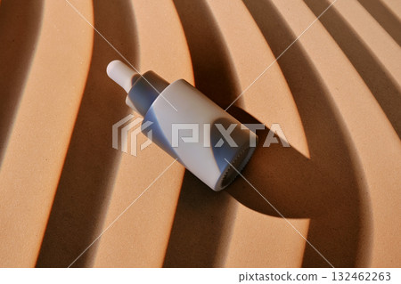 A bottle of serum on a beige background with stripes of shadows. A bottle of serum on a beige background with stripes of shadows. 132462263
