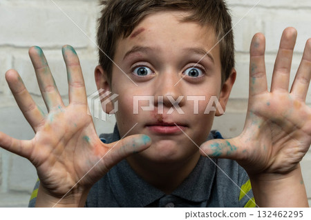 Young boy with messy hands covered in colorful paint, displaying a playful expression, showcasing creativity and joy in an artistic environment with a textured background Young boy with messy hands covered in colorful paint, displaying a playful expression, showcasing creativity and joy in an artistic environment with a textured background 132462295