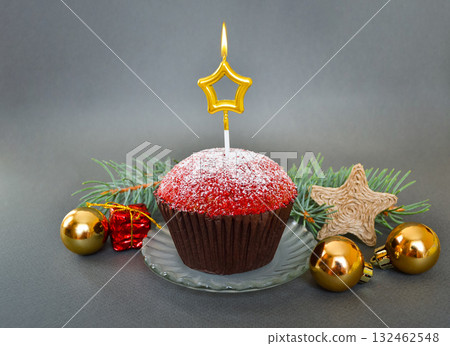 Christmas composition with a cupcake and a candle, on a gray background. Christmas composition with a cupcake and a candle, on a gray background. 132462548