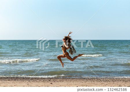 Beach girl leap, Joyful female jumps during sunny day, Vibrant woman executing athletic jump along sunlit shoreline Beach girl leap, Joyful female jumps during sunny day, Vibrant woman executing athletic jump along sunlit shoreline 132462586