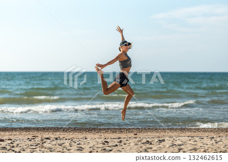 Dynamic leap by shoreline under midday sky, Midair woman performing vigorous coastal workout in bright sunlight 132462615