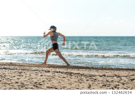 Athlete runs on shoreline sands, Competitor accelerates along damp coast as waves crash and sunlight illuminates scene Athlete runs on shoreline sands, Competitor accelerates along damp coast as waves crash and sunlight illuminates scene 132462634