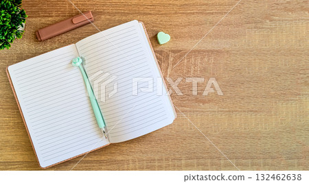 There is an open notebook with a pen and erasers on the wooden surface of the table. There is an open notebook with a pen and erasers on the wooden surface of the table. 132462638
