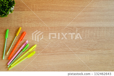 Colored pens lie on a wooden table. A flower is in the background. Colored pens lie on a wooden table. A flower is in the background. 132462643