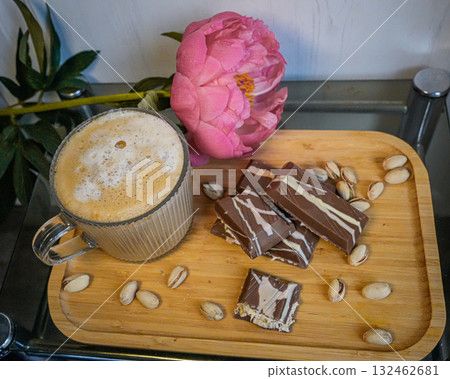 Cup of coffee with foam, chocolate bars, cashew nuts, and a small flower on a wooden tray. Cup of coffee with foam, chocolate bars, cashew nuts, and a small flower on a wooden tray. 132462681