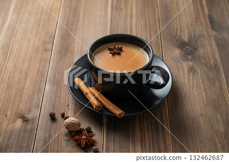 Traditional Indian masala chai tea with milk and spices in a black cup on a dark wooden background 132462687