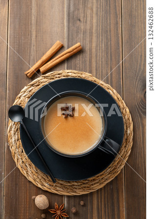 Traditional Indian masala chai tea with milk and spices in a black cup on a dark wooden background Traditional Indian masala chai tea with milk and spices in a black cup on a dark wooden background 132462688