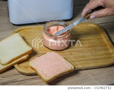 Hand scooping creamy spread from a jar next to a slice of bread on a wooden tray. Hand scooping creamy spread from a jar next to a slice of bread on a wooden tray. 132462732