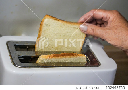 Hand holding a slice of toasted bread while taking it out of a toaster. Hand holding a slice of toasted bread while taking it out of a toaster. 132462733