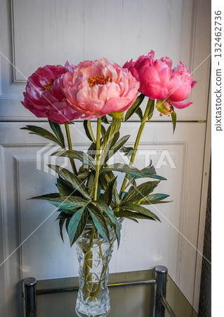 Medium shot of pink peonies in a clear glass vase on a table. Medium shot of pink peonies in a clear glass vase on a table. 132462736