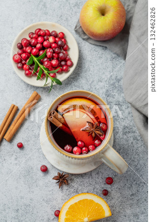 A hot cranberry Christmas drink in a mug on a gray background with cinnamon, berries and fruits. A hot cranberry Christmas drink in a mug on a gray background with cinnamon, berries and fruits. 132462826