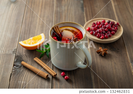 A mulled wine in a mug with cinnamon, berries and fruits on a dark wooden background. A mulled wine in a mug with cinnamon, berries and fruits on a dark wooden background. 132462831