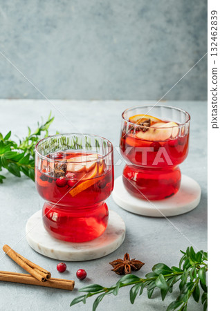 A cranberry drink in a two glasses on a light background with cinnamon and green branch. A cranberry drink in a two glasses on a light background with cinnamon and green branch. 132462839