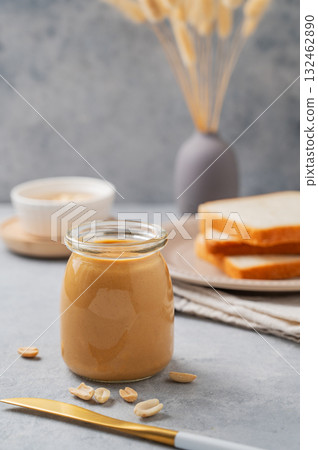 Creamy peanut butter in a jar on a blue background with a scattering of roasted nuts, knife Creamy peanut butter in a jar on a blue background with a scattering of roasted nuts, knife 132462890