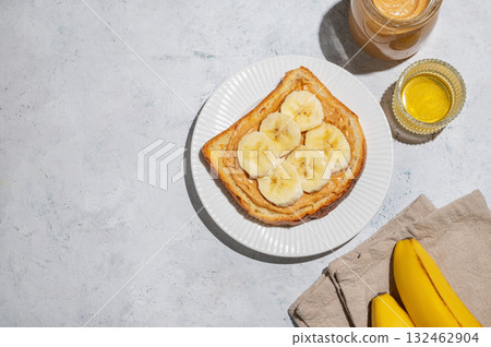Peanut butter toast with banana on a plate on a light background with spread, fruit, honey Peanut butter toast with banana on a plate on a light background with spread, fruit, honey 132462904