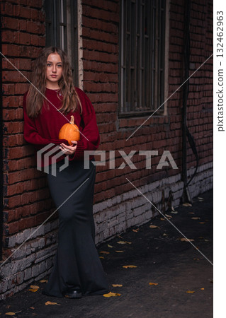 Teen girl in a red sweater holds a pumpkin while leaning against an old brick wall with autumn leaves on the ground in the Timiryazevs Academy, Moscow Teen girl in a red sweater holds a pumpkin while leaning against an old brick wall with autumn leaves on the ground in the Timiryazevs Academy, Moscow 132462963