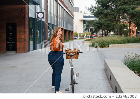Female city commuter walking with bike to office. 132463008