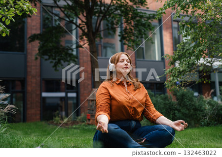 Beautiful mid size woman meditating in park, listening podcast. 132463022