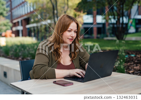 Plus size woman working on laptop outdoors. 132463031