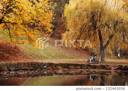 Son and older father sitting on bench by lake and talking. Son and older father sitting on bench by lake and talking. 132463036