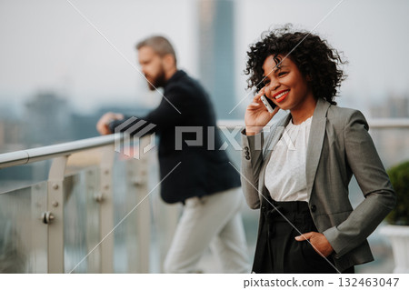 A businesswoman standing on terrace in modern office, making phone call. Panorama view behind. A businesswoman standing on terrace in modern office, making phone call. Panorama view behind. 132463047