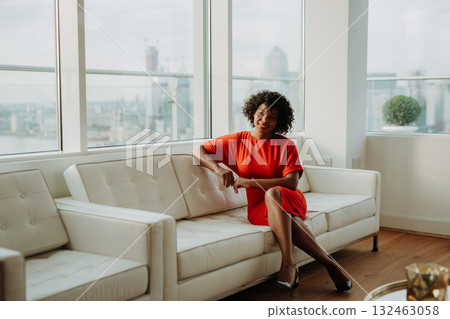 Businesswoman in red dress sitting on sofa in modern office. London view panorama. Businesswoman in red dress sitting on sofa in modern office. London view panorama. 132463058