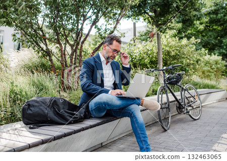 Manager working in urban park, making phone call and typing on laptop. 132463065
