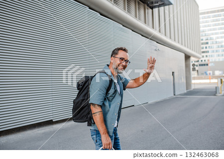 Handsome man with tattoos greeting someone on street. 132463068