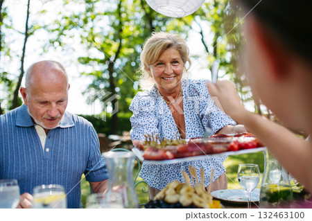 Senior woman serving grilled food during family grill party. Senior woman serving grilled food during family grill party. 132463100