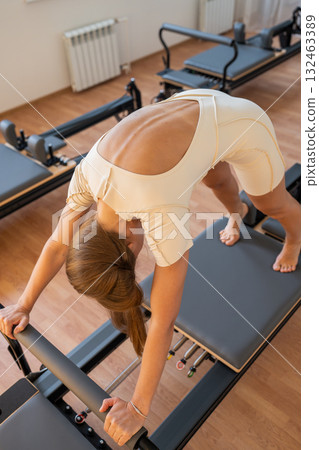 Pilates Woman showcases deep hamstring stretch, reformer exercise emphasizing hamstrings and breath control Pilates Woman showcases deep hamstring stretch, reformer exercise emphasizing hamstrings and breath control 132463389