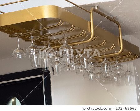 Hanging wine glasses on golden rack in bar interior. Refined composition, transparency, and elegant geometric design. 132463663
