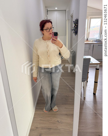 Woman in beige cardigan and gray jeans taking mirror selfie at home. Cozy mood, neutral tones, and relaxed modern lifestyle. Woman in beige cardigan and gray jeans taking mirror selfie at home. Cozy mood, neutral tones, and relaxed modern lifestyle. 132463671