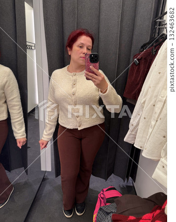 Woman trying on beige cardigan and brown trousers in fitting room. Cozy fabric, minimal design and neutral fashion palette. Woman trying on beige cardigan and brown trousers in fitting room. Cozy fabric, minimal design and neutral fashion palette. 132463682