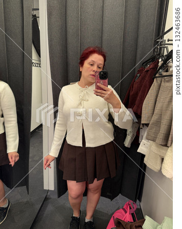 Woman in white cardigan adjusting outfit in fitting room. Style exploration, mirror reflection, and fashion decision moment. Woman in white cardigan adjusting outfit in fitting room. Style exploration, mirror reflection, and fashion decision moment. 132463686