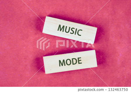 Two wooden blocks lay on a pink surface, spelling out MUSIC MODE. A call to explore the auditory world and let the rhythm influence your choices 132463750
