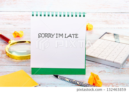 A desk displays a spiral notepad reading Sorry Im Late. A calculator, pen, magnifying glass, sticky note, and crumpled paper add to the scene, suggesting a busy day 132463859