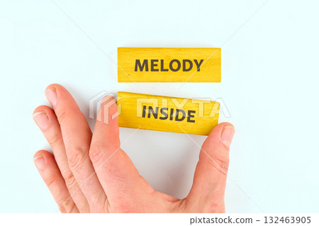 A hand gently reaches for colorful wooden blocks arranged to display the words melody inside. The bright yellow color creates a cheerful atmosphere and inspires creativity A hand gently reaches for colorful wooden blocks arranged to display the words melody inside. The bright yellow color creates a cheerful atmosphere and inspires creativity 132463905