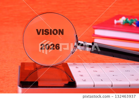 A magnifying glass focuses on the words Vision 2026, placed on a calculator. Bright colored stationery adds a creative touch to the workspace, symbolizing planning and foresight 132463937