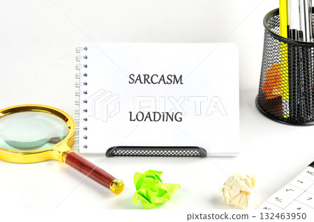 A quirky desk scene features a notebook declaring sarcasm loading, complemented by colorful paper balls, a magnifying glass, and vibrant stationery for a playful atmosphere 132463950