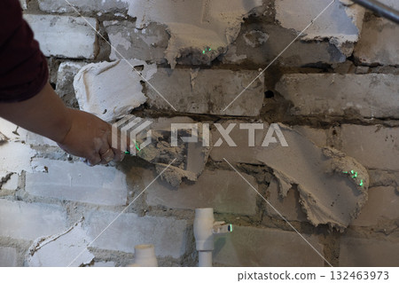 A worker holds a trowel and applies wet plaster or filler mix to an old brick wall during renovation, remodeling, or construction, improving the surface. Preparing a wall with filler. A worker holds a trowel and applies wet plaster or filler mix to an old brick wall during renovation, remodeling, or construction, improving the surface. Preparing a wall with filler. 132463973