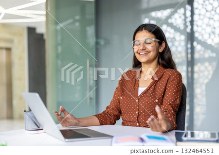 Young indian corporate professional finding inner peace and mindful balance at her office desk, practicing meditation and relaxation in a modern workspace Young indian corporate professional finding inner peace and mindful balance at her office desk, practicing meditation and relaxation in a modern workspace 132464551